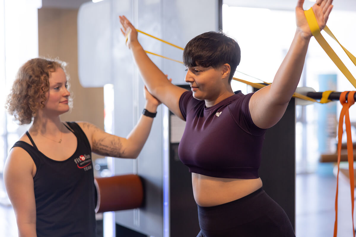 Gesundheitstraining Betreuung mit Mitglied und Trainerin bei einer Übung mit Dehn-Bändern im Fit 'n Fun Gau-Algesheim bei Ingelheim